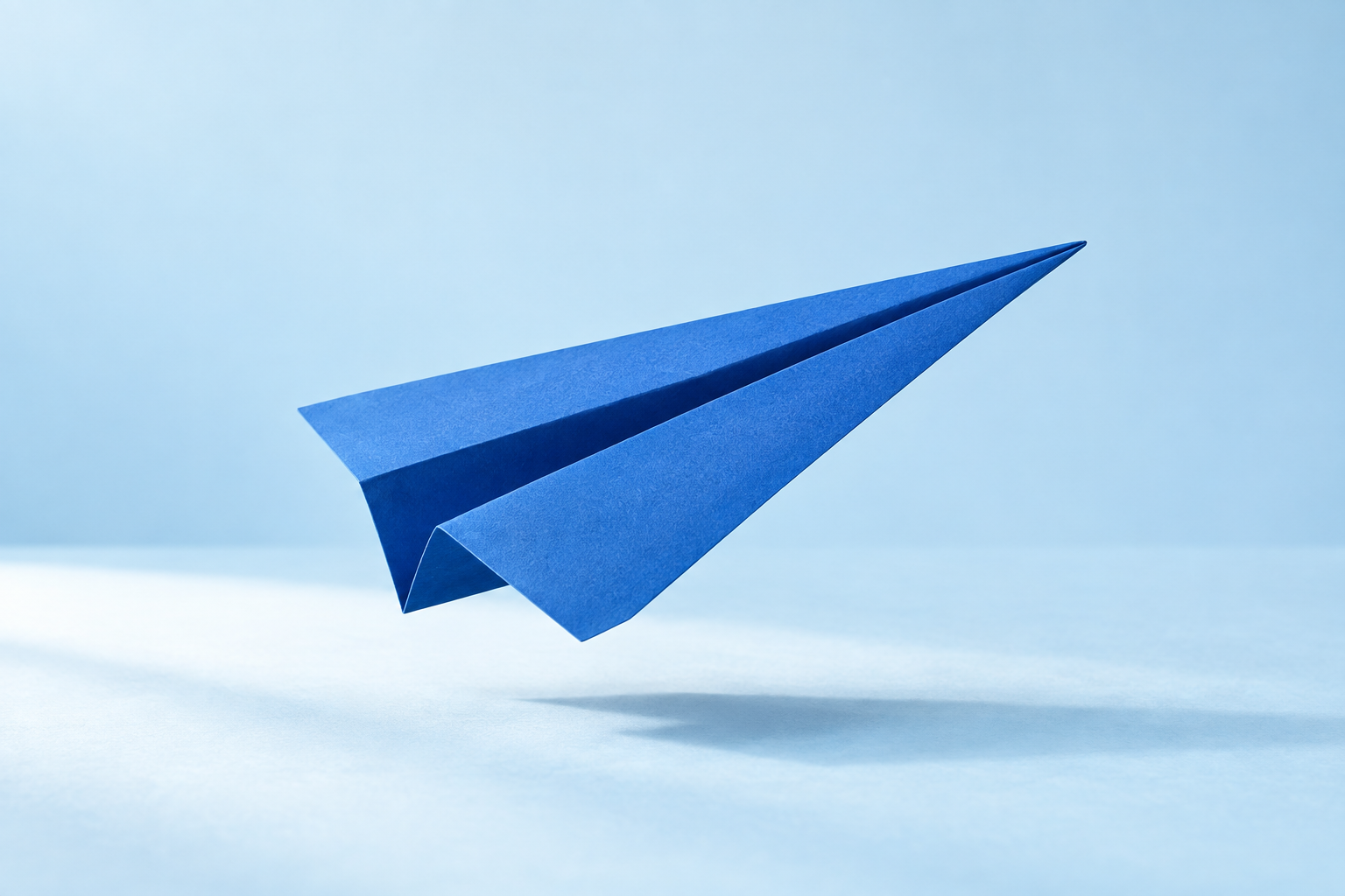 A cobalt-blue paper airplane lifting into the light